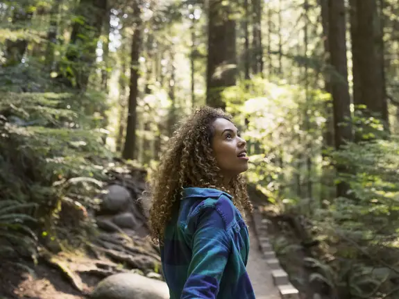 young woman hiking in the woods, looking up in awe